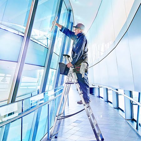 A facilities maintenance worker cleaning windows in a high-tech environment